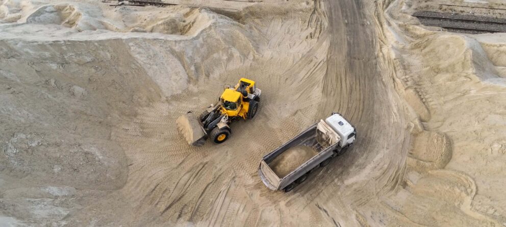 Big heavy wheel loader loading sand into dump truck in sand pit. Heavy industrial machinery concept.