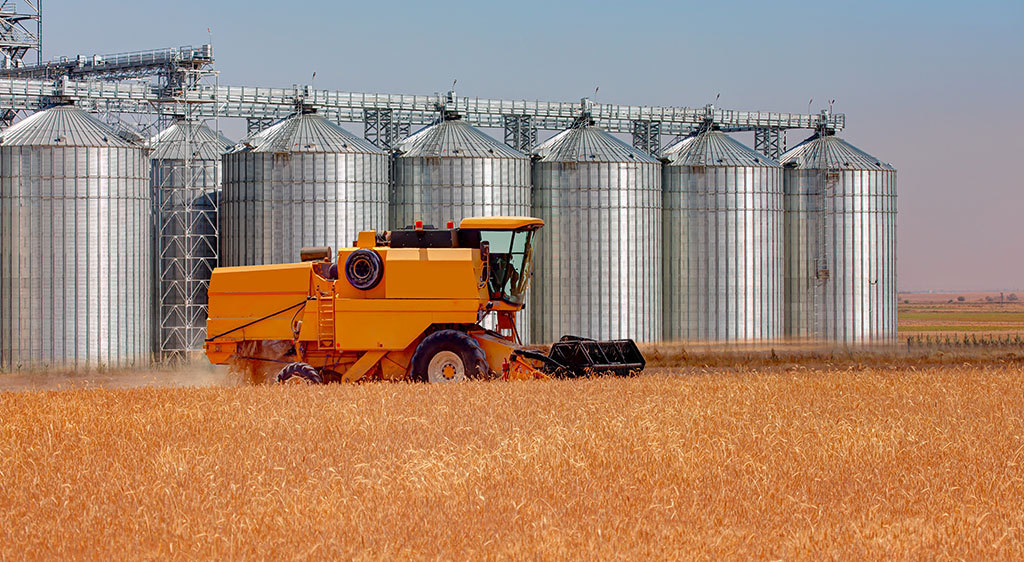 an agricultural machine in a cornfield in front of silos